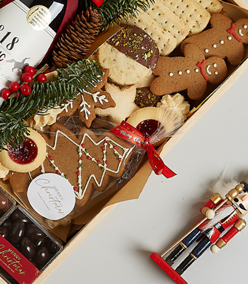 Festive gift box featuring Signus Classic Red Wine, cookies, gingerbread, and holiday-themed decorations, including greenery and nutcracker ornaments.