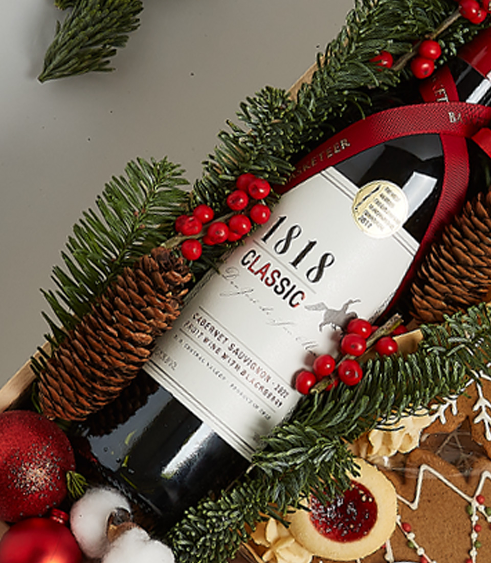 Festive gift box featuring Signus Classic Red Wine, cookies, gingerbread, and holiday-themed decorations, including greenery and nutcracker ornaments.