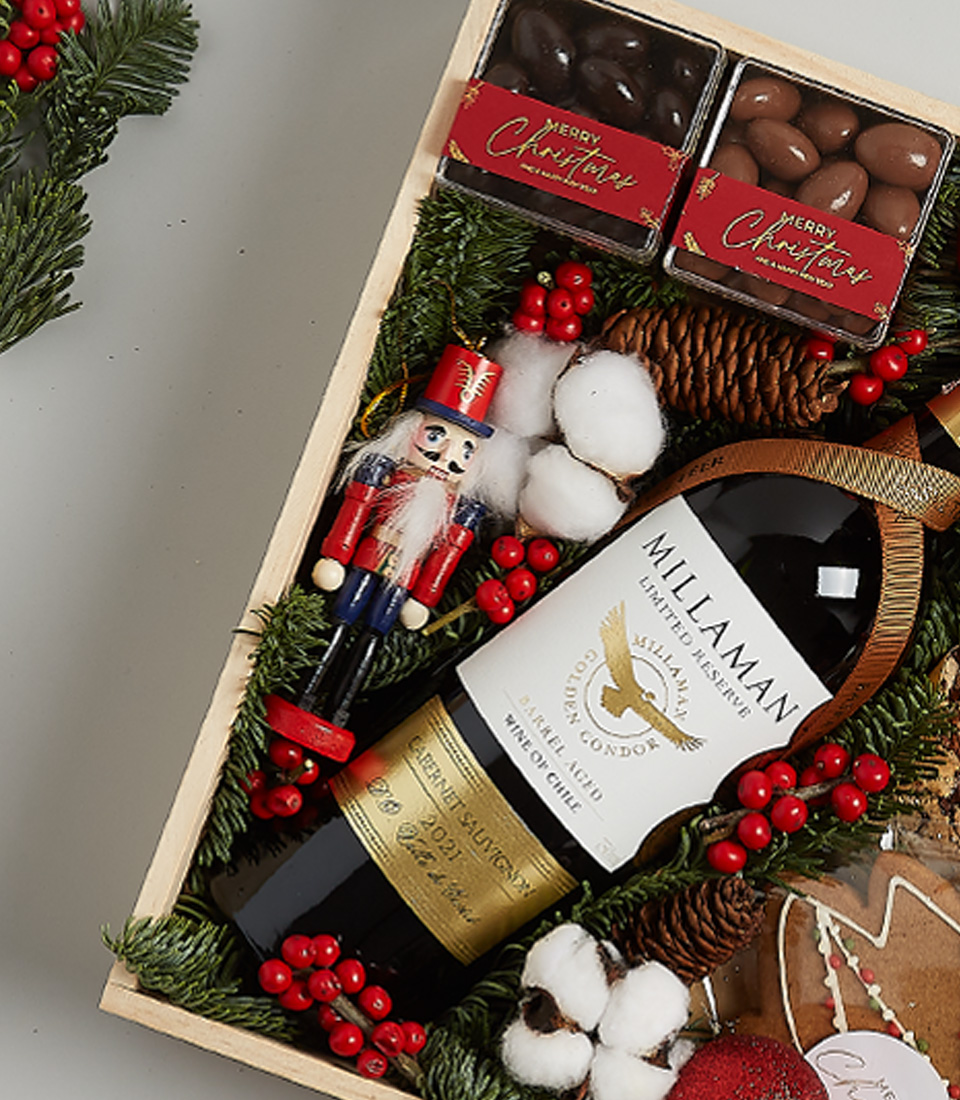 Christmas gift box with William Fevre Chardonnay, gingerbread cookies, chocolates, shortbread biscuits, festive greenery, and a nutcracker ornament.