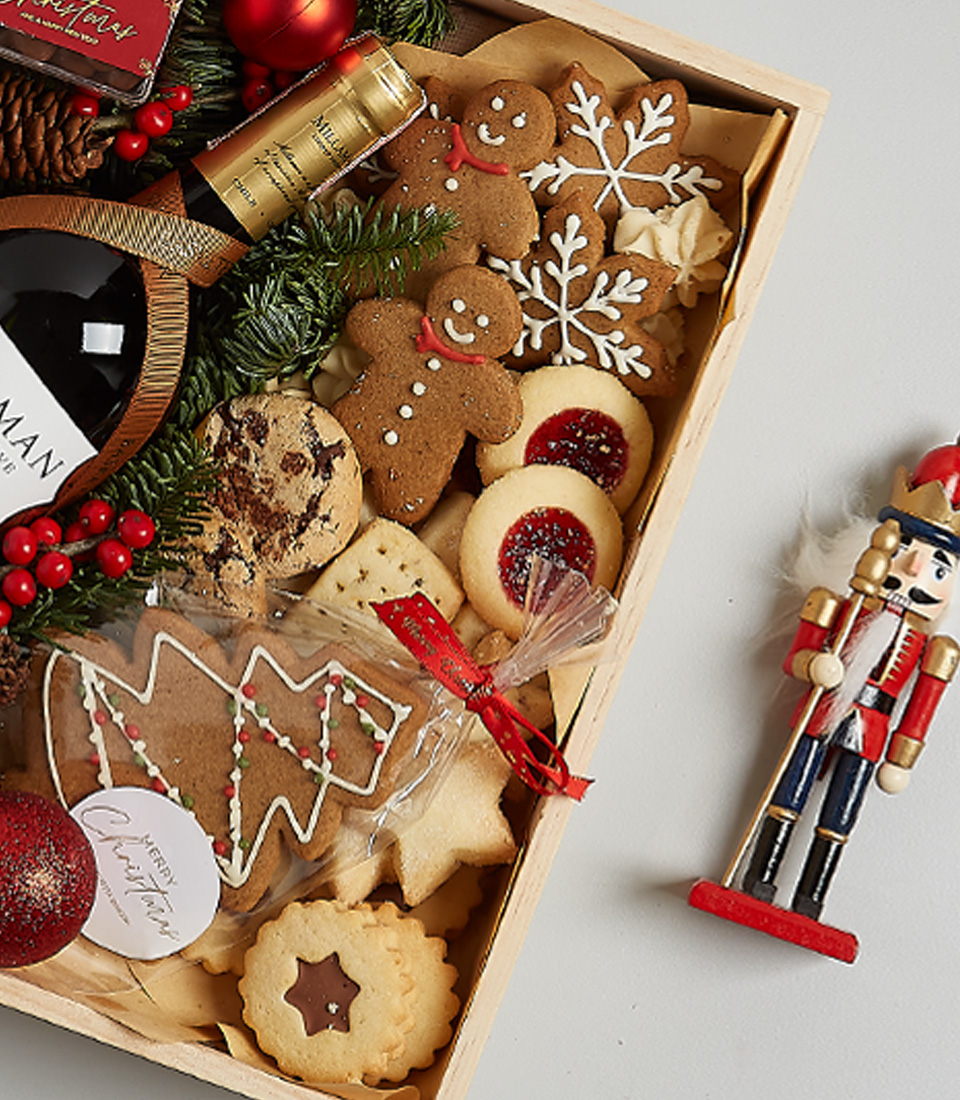 Christmas gift box with William Fevre Chardonnay, gingerbread cookies, chocolates, shortbread biscuits, festive greenery, and a nutcracker ornament.