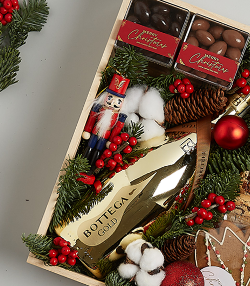Festive gift box featuring Bottega Gold Prosecco, gingerbread cookies, chocolates, shortbread, holiday greenery, and nutcracker decoration.