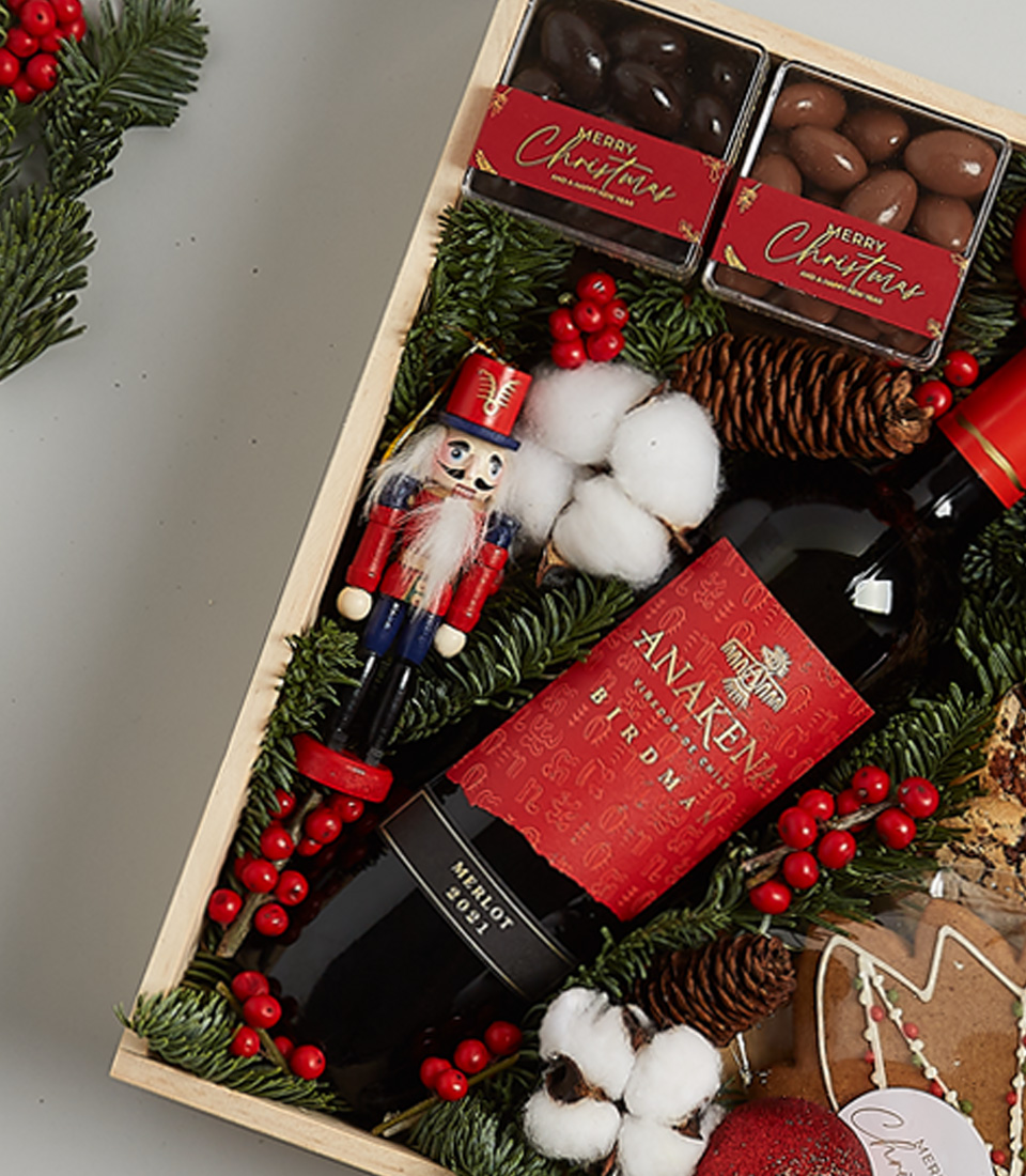 Elegant Christmas gift box featuring Anakena Merlot wine, gingerbread cookies, chocolates, shortbread, holiday greenery, and a nutcracker decoration.