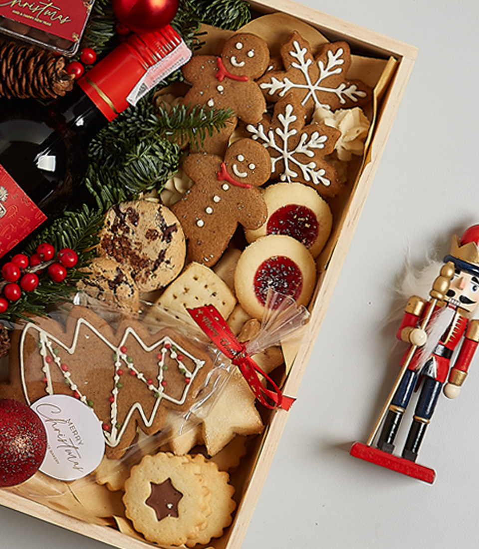 Elegant Christmas gift box featuring Anakena Merlot wine, gingerbread cookies, chocolates, shortbread, holiday greenery, and a nutcracker decoration.