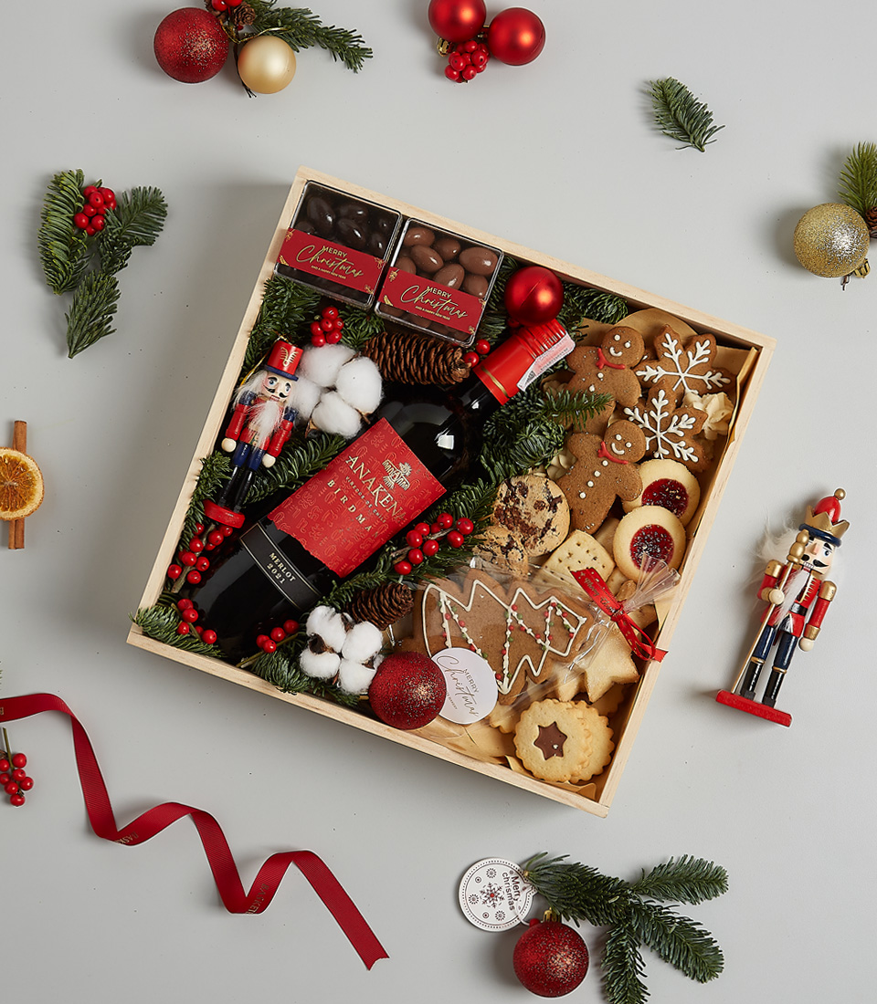 Elegant Christmas gift box featuring Anakena Merlot wine, gingerbread cookies, chocolates, shortbread, holiday greenery, and a nutcracker decoration.