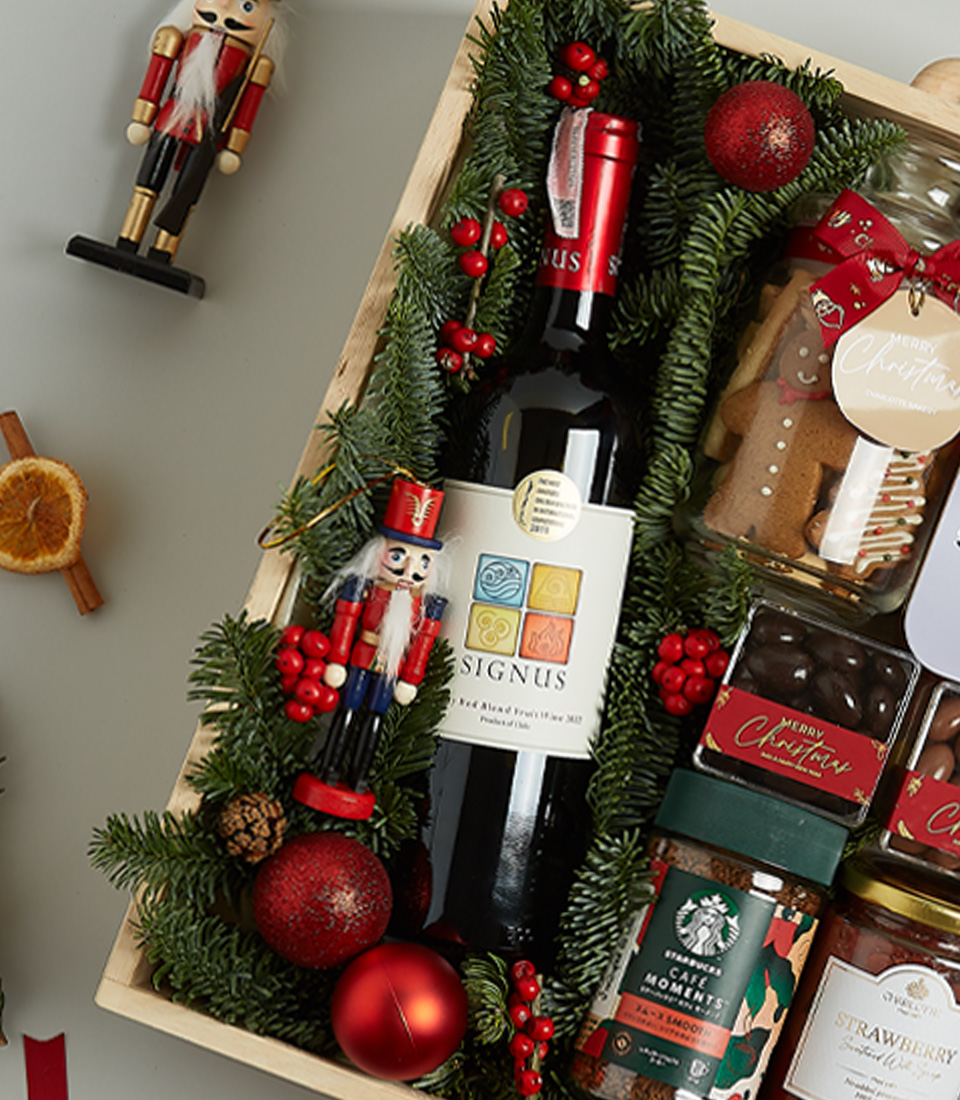 Christmas gift hamper featuring Signus wine, shortbread biscuits, chocolates, preserves, and festive decorations in a wooden box.