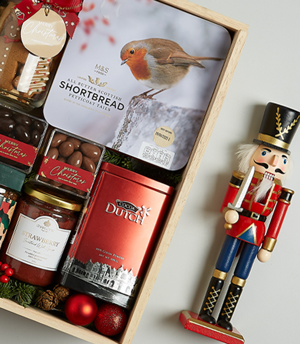 Christmas gift hamper featuring Signus wine, shortbread biscuits, chocolates, preserves, and festive decorations in a wooden box.
