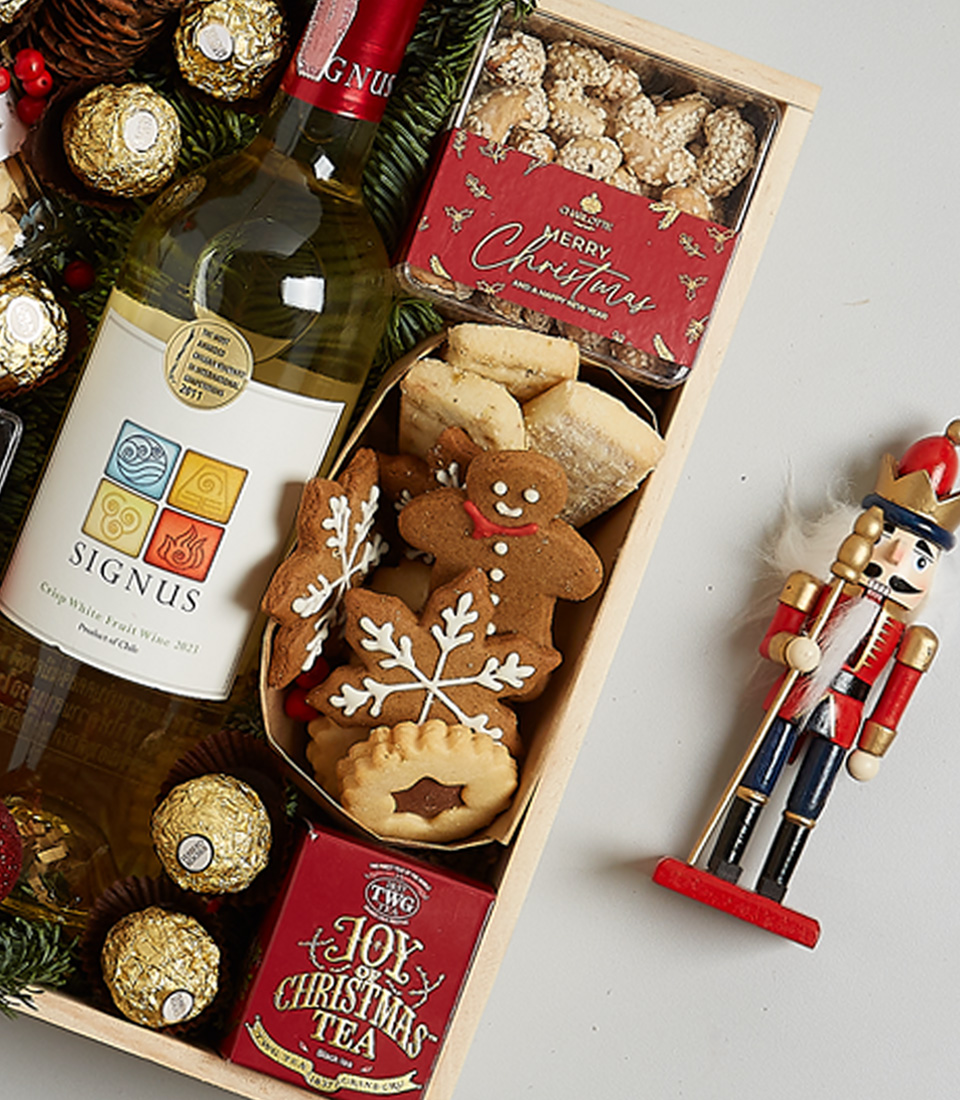 Christmas gift hamper featuring Signus white wine, Ferrero Rocher chocolates, mince pies, gingerbread cookies, and festive greenery with ornaments.