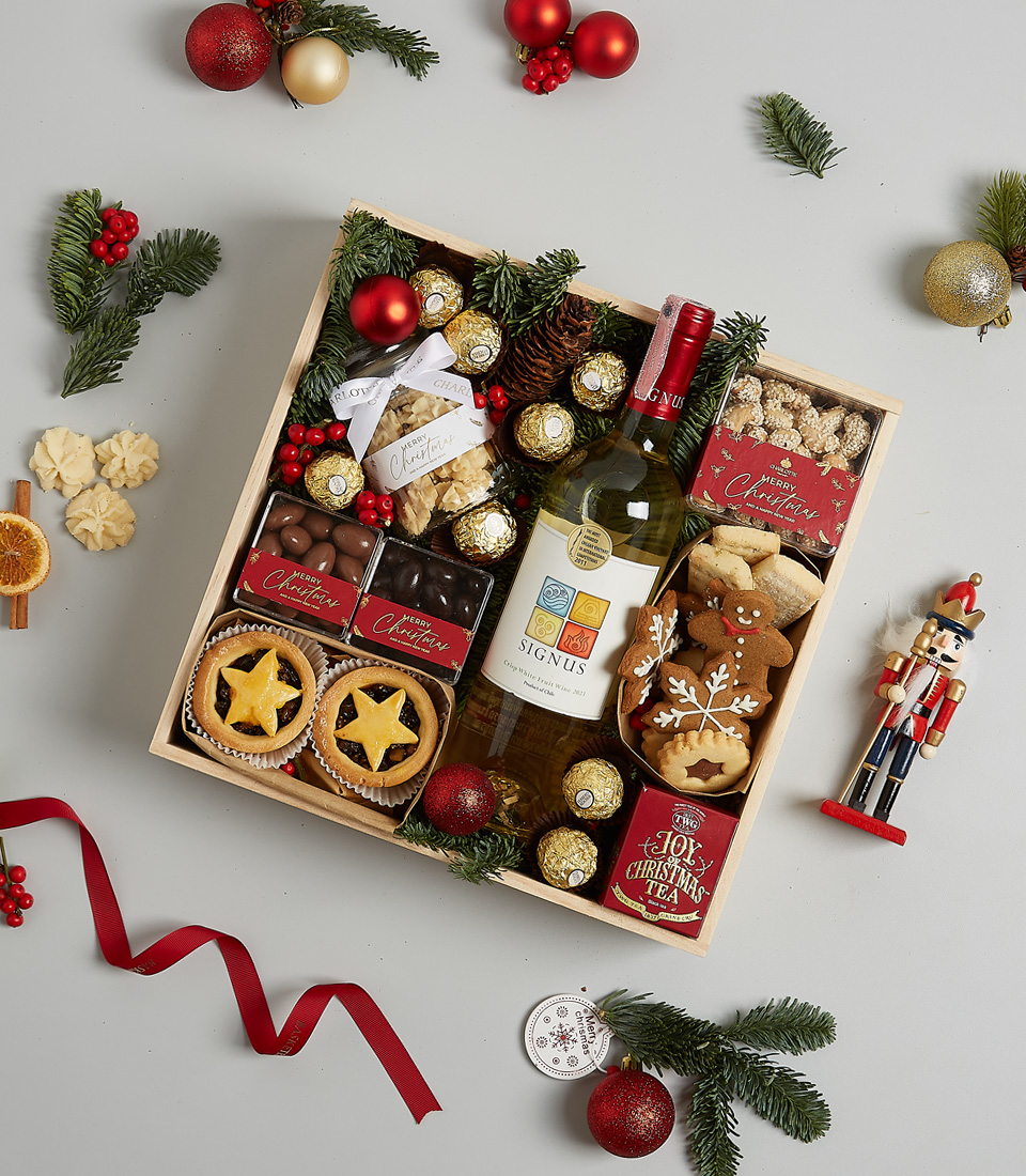 Christmas gift hamper featuring Signus white wine, Ferrero Rocher chocolates, mince pies, gingerbread cookies, and festive greenery with ornaments.