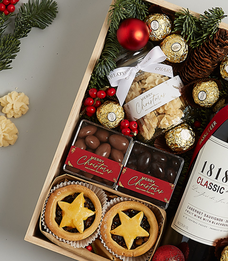 Elegant Christmas gift box with 1818 Classic Red Wine, Ferrero Rocher chocolates, mince pies, gingerbread cookies, and holiday decorations.