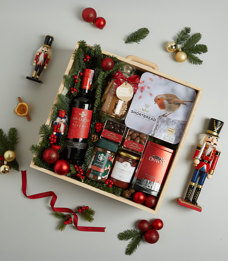 Holiday hamper with Anakena red wine, Christmas pudding, shortbread, chocolates, preserves, and festive decorations in a wooden box.