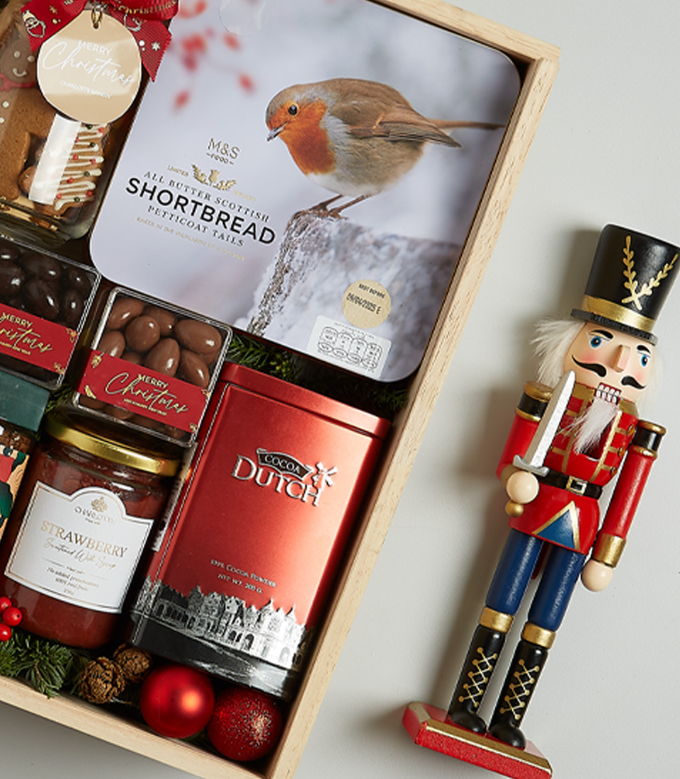 Holiday hamper with Anakena red wine, Christmas pudding, shortbread, chocolates, preserves, and festive decorations in a wooden box.