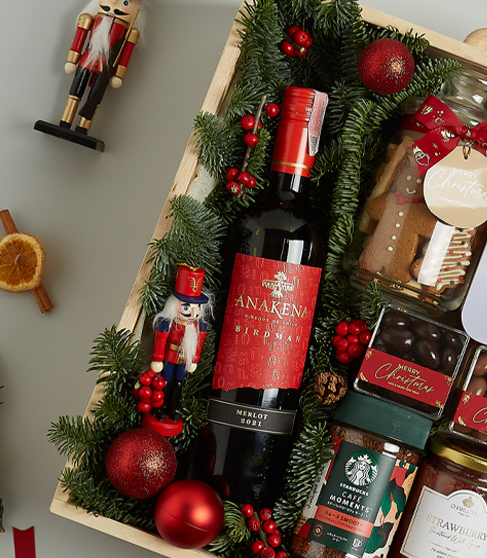 Holiday hamper with Anakena red wine, Christmas pudding, shortbread, chocolates, preserves, and festive decorations in a wooden box.