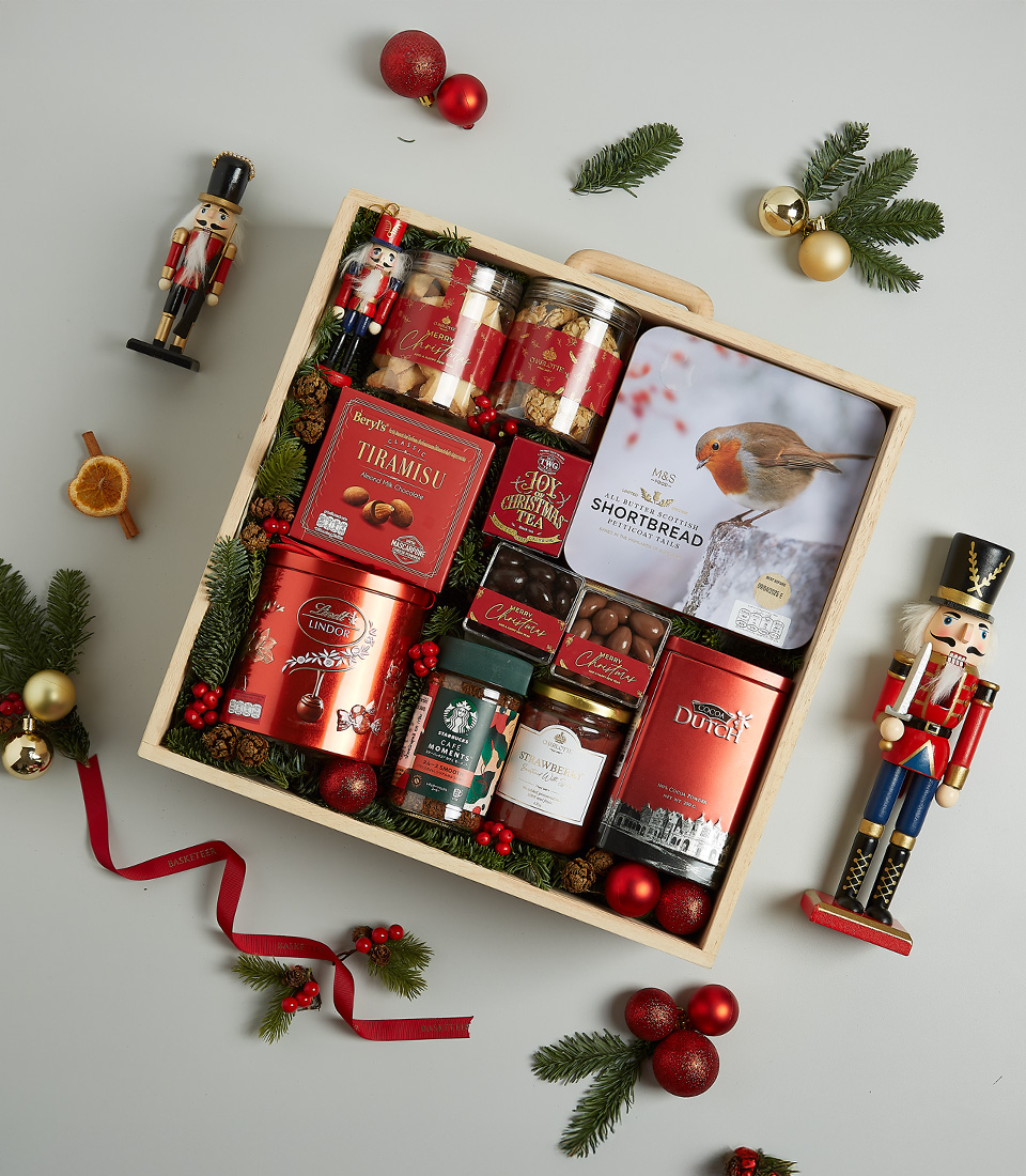Festive wooden Christmas hamper filled with tiramisu cookies, shortbread, chocolates, jams, Christmas pudding, and holiday decorations.