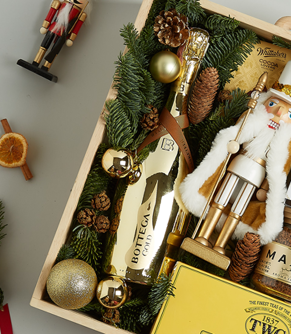 Christmas gift hamper with TWG tea, Bottega Gold prosecco, cookies, honey, gourmet spreads, and a nutcracker figurine in a festive wooden box.