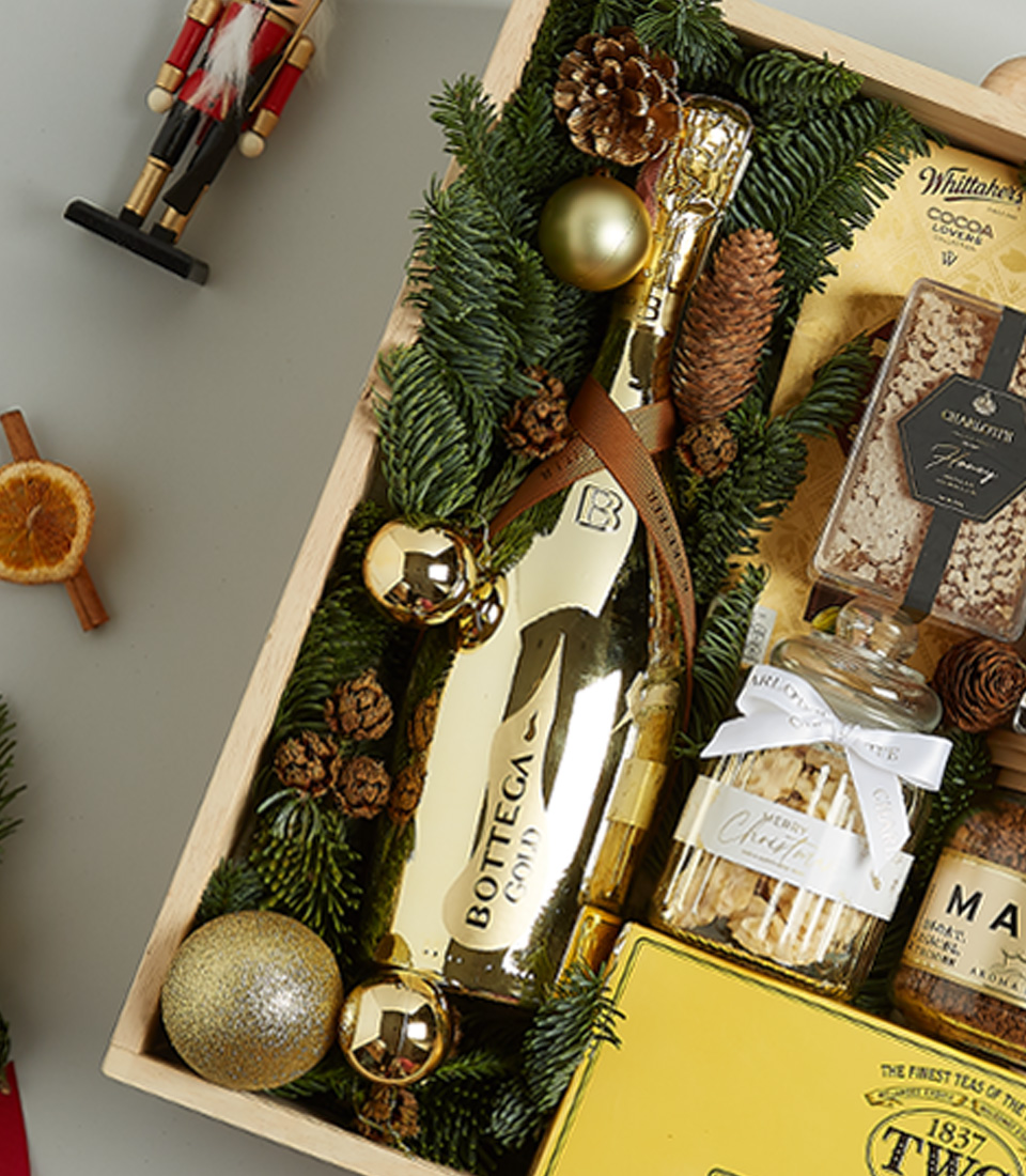 Holiday gift box with TWG tea, Bottega Gold prosecco, artisanal cookies, chocolate, honey, and spreads in a decorative festive arrangement.