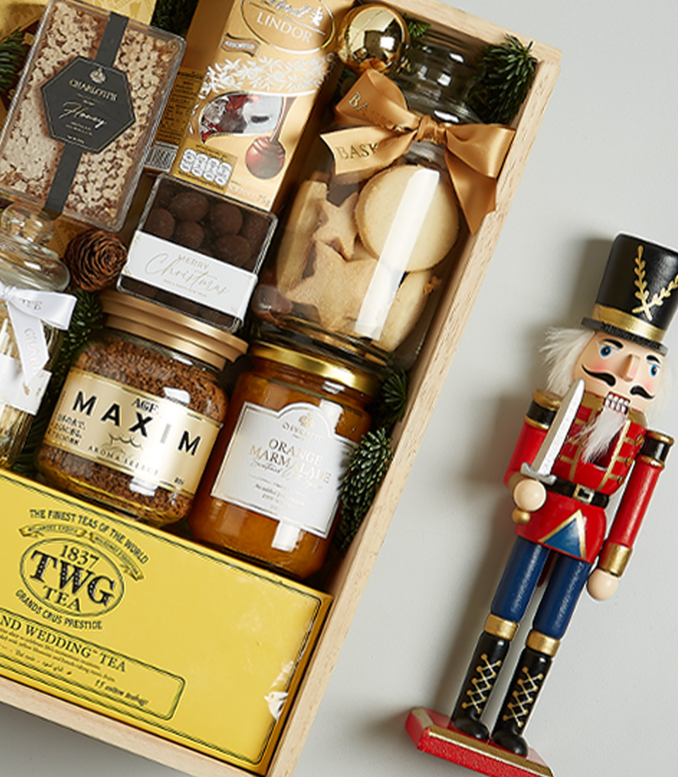 Holiday gift box with TWG tea, Bottega Gold prosecco, artisanal cookies, chocolate, honey, and spreads in a decorative festive arrangement.