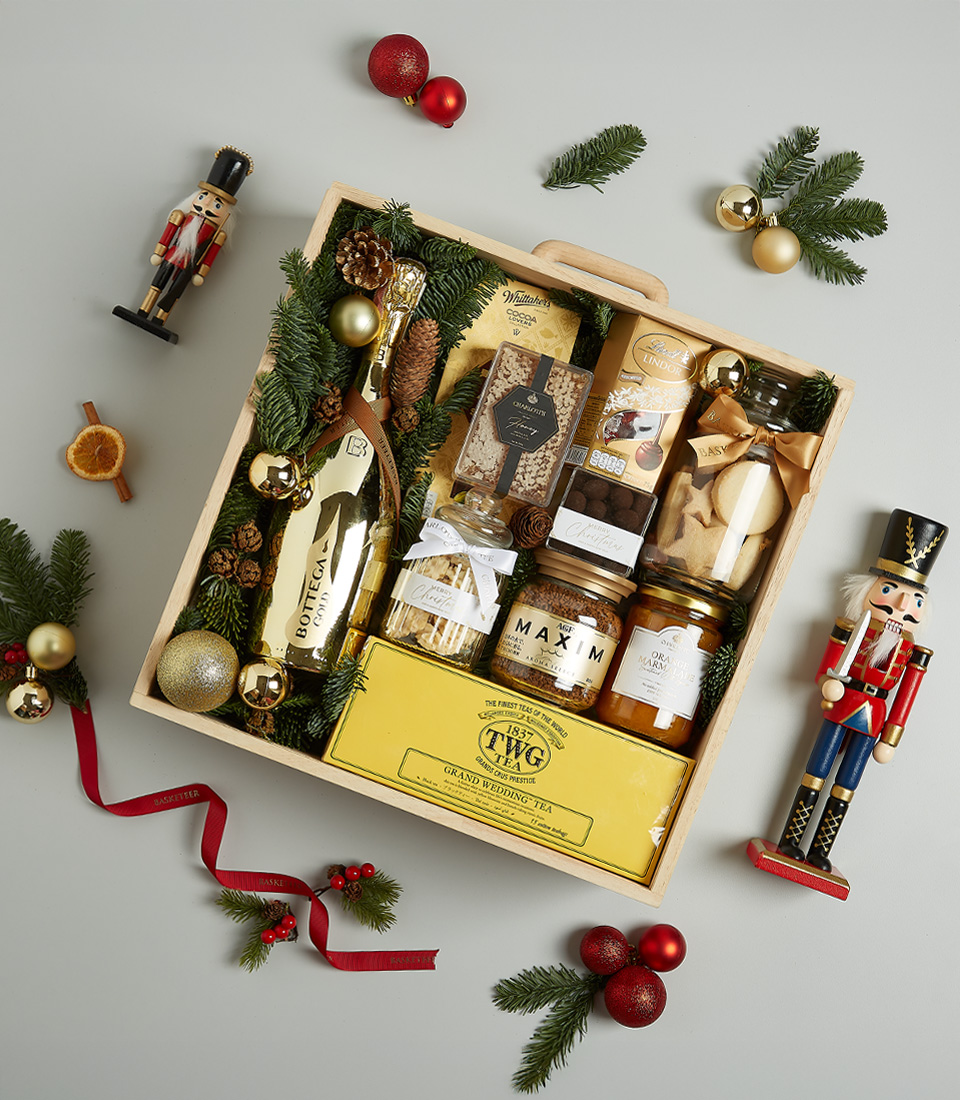 Holiday gift box with TWG tea, Bottega Gold prosecco, artisanal cookies, chocolate, honey, and spreads in a decorative festive arrangement.
