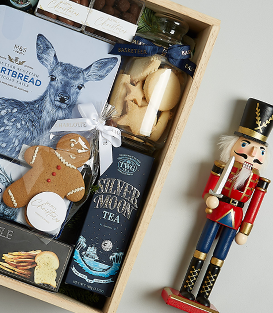 Luxury Christmas gift hamper with sparkling wine, shortbread, truffle crisps, Silver Moon tea, and gingerbread, decorated with blue and festive ornaments.