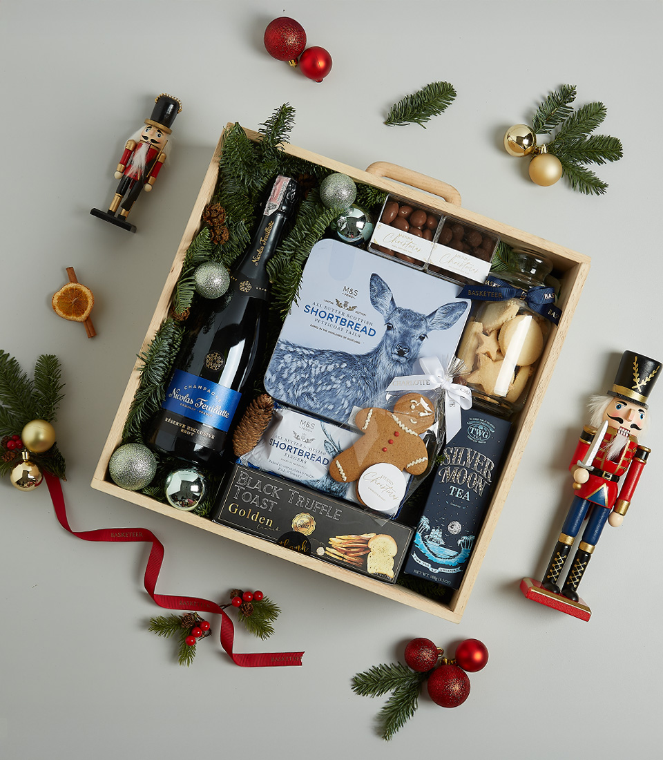 Luxury Christmas gift hamper with sparkling wine, shortbread, truffle crisps, Silver Moon tea, and gingerbread, decorated with blue and festive ornaments.