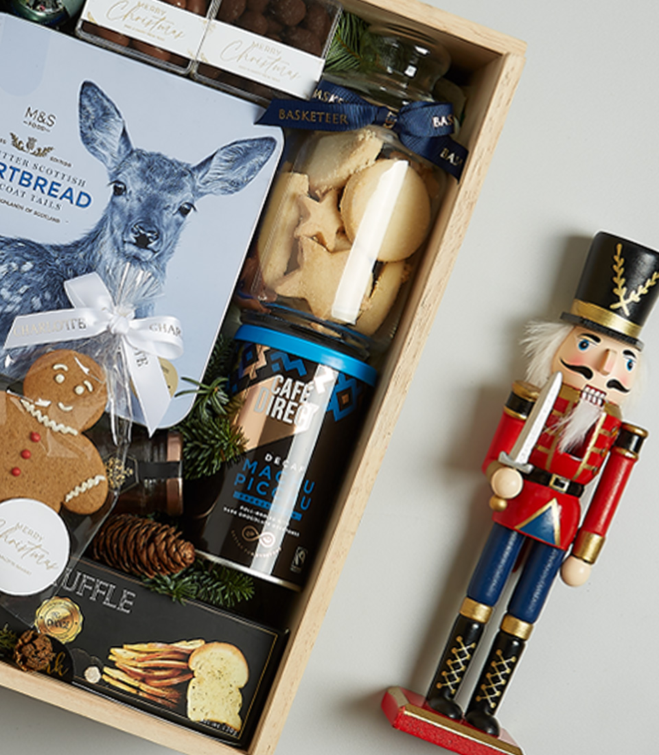Elegant Christmas gift hamper containing Solar Viejo red wine, shortbread cookies, black truffle crisps, chocolate almonds, Silver Moon tea, and a gingerbread cookie in festive blue and silver accents.
