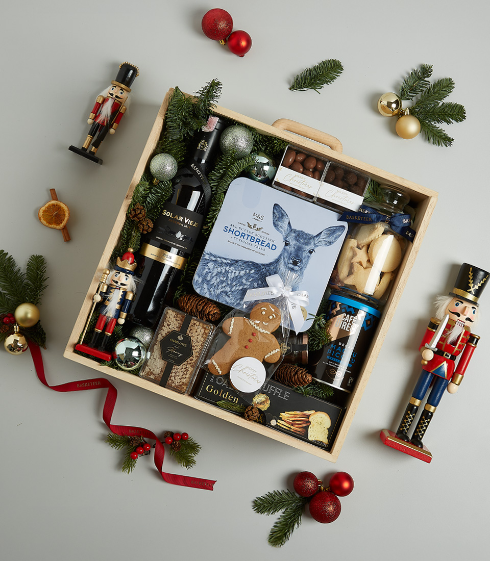 Elegant Christmas gift hamper containing Solar Viejo red wine, shortbread cookies, black truffle crisps, chocolate almonds, Silver Moon tea, and a gingerbread cookie in festive blue and silver accents.