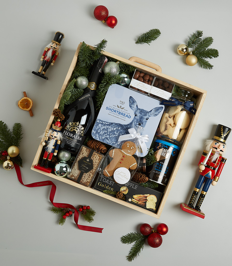 Premium Christmas gift hamper with Floralba sparkling wine, shortbread cookies, truffle crisps, Silver Moon tea, chocolate almonds, and festive gingerbread cookies, arranged in blue and silver holiday decor.