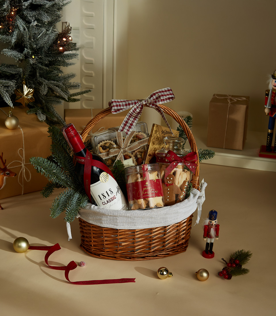 Holiday gift basket with 1818 Classic Red Wine, festive shortbread cookies, gourmet chocolates, and snacks in a decorated wicker basket with ribbon and holiday decor.