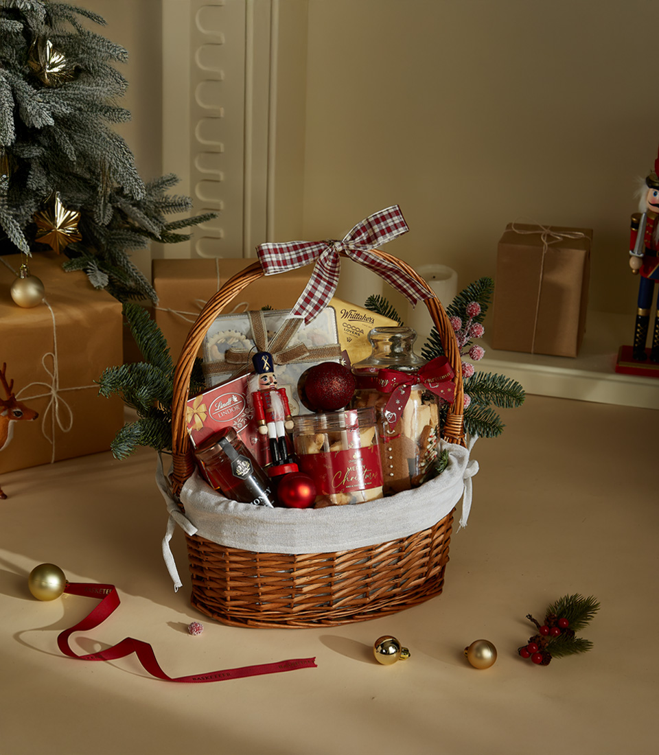 Christmas gift basket with festive cookies, chocolates, a nutcracker figurine, and holiday decorations arranged in a wicker basket with ribbon accents.