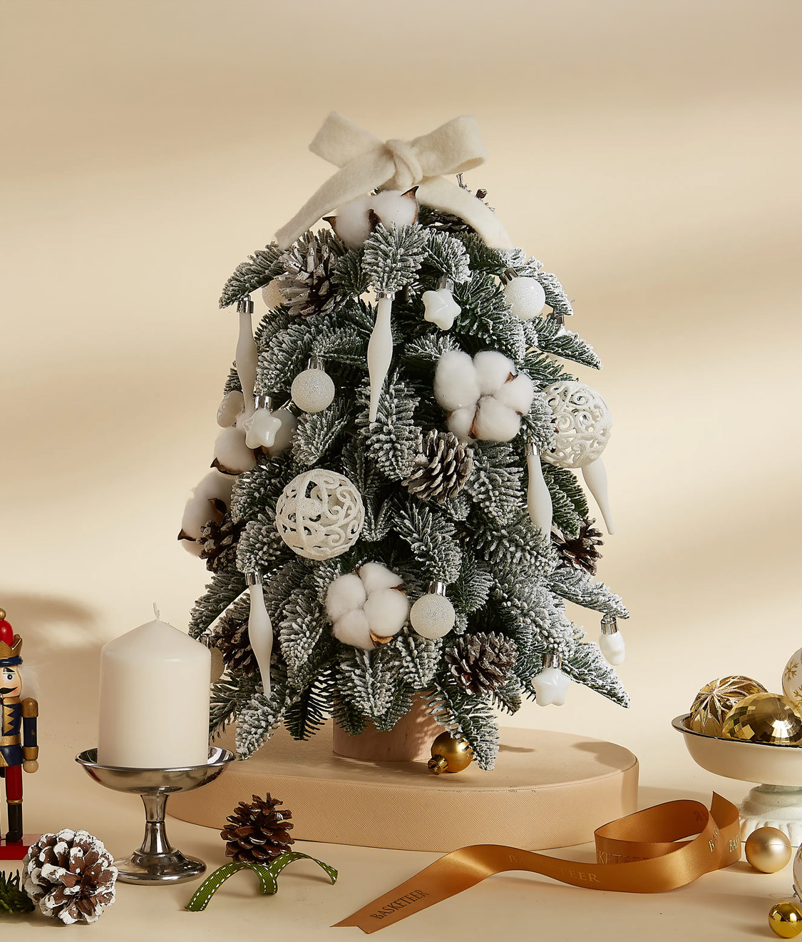 A charming mini Christmas tree adorned with white ornaments, cotton accents, pinecones, and a bow topper, perfect for festive decor.
