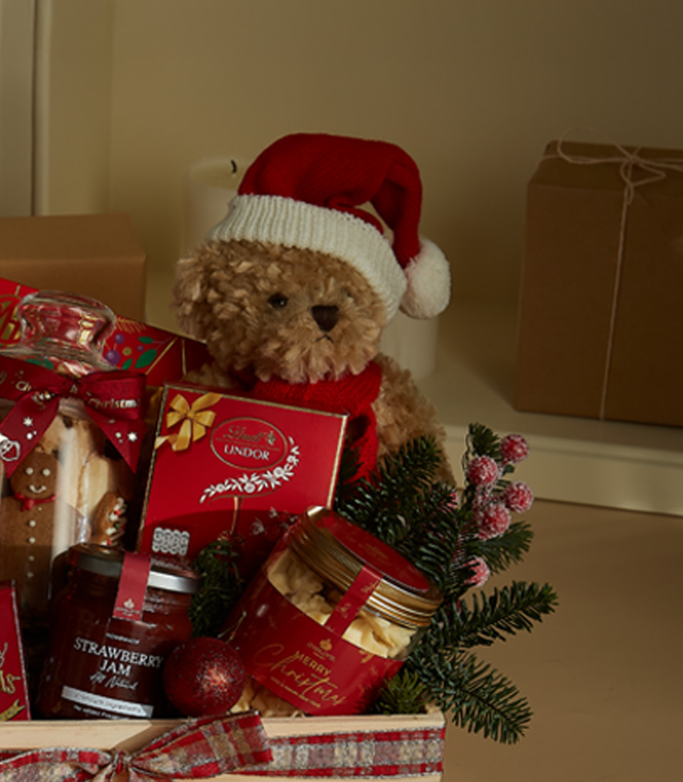 Festive wooden gift hamper featuring Lindt chocolates, holiday cookies, Christmas tea, strawberry preserves, and a plush Santa bear.