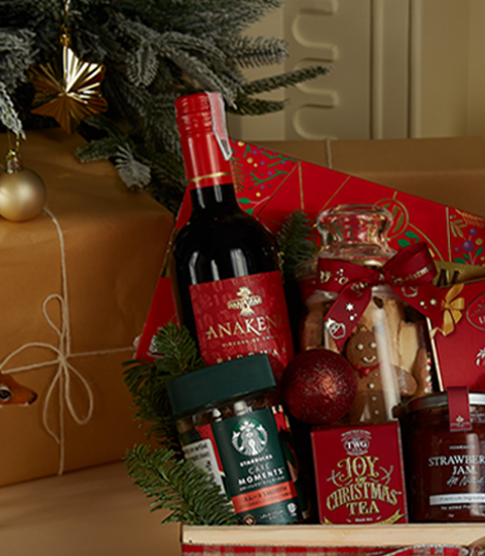 Christmas wooden gift hamper featuring a bottle of Anakena wine, holiday cookies, Christmas tea, strawberry preserves, chocolates, and a festive plush Santa bear.