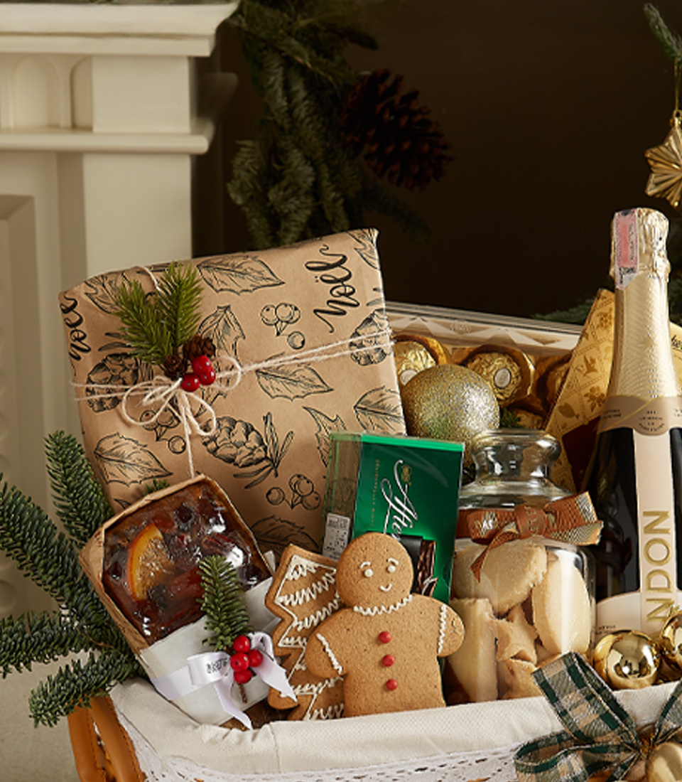 Elegant Christmas gift basket with Chandon sparkling wine, gingerbread cookies, fruitcake, mince pies, and seasonal decorations in a wicker basket.