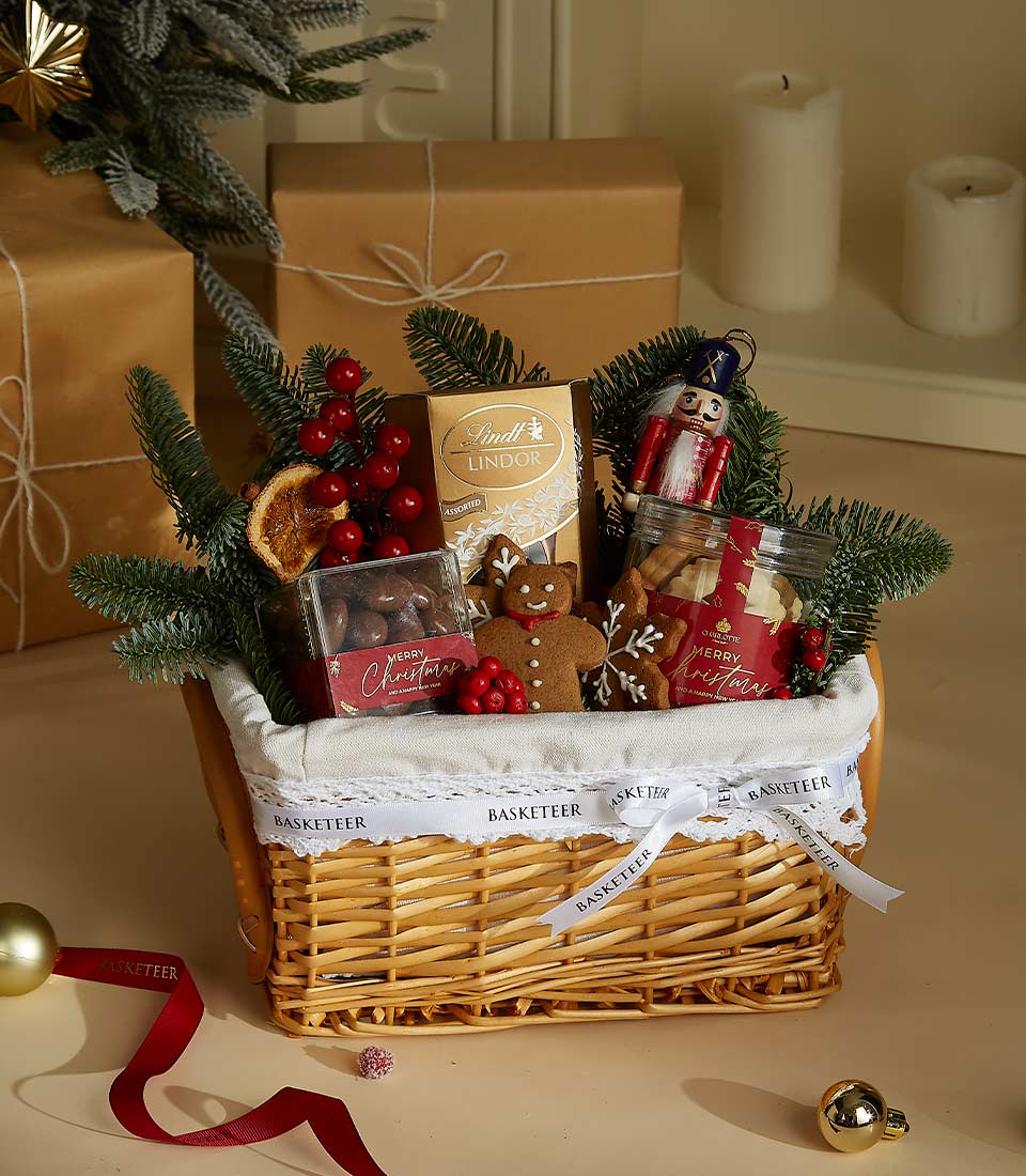 Mini holiday gift basket with Lindt chocolates, a gingerbread cookie, festive nuts, and a decorative nutcracker figurine, presented in a wicker basket.