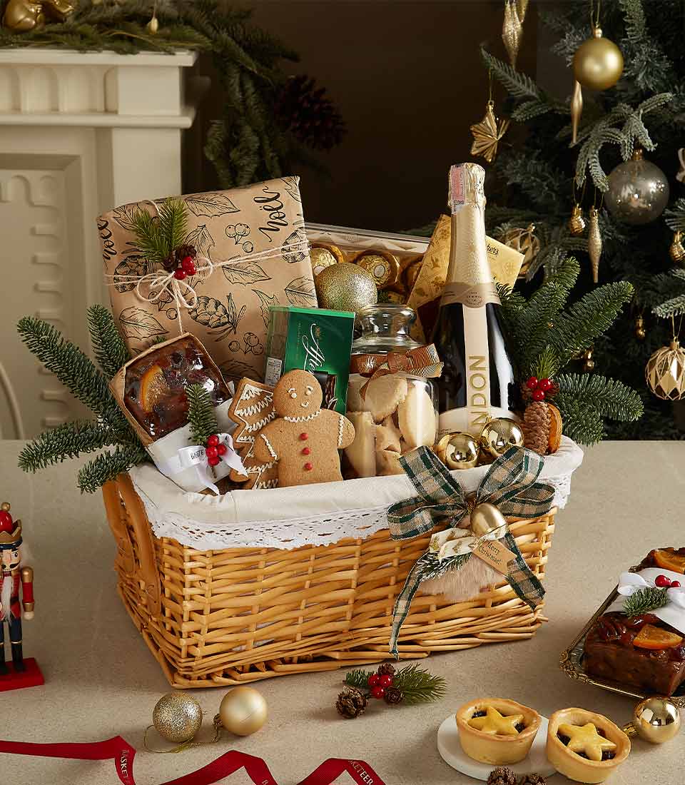 Elegant Christmas gift basket with Chandon sparkling wine, gingerbread cookies, fruitcake, mince pies, and seasonal decorations in a wicker basket.