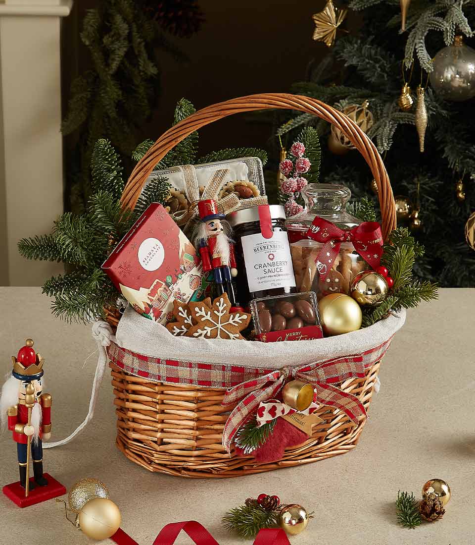 Holiday wicker basket with cranberry sauce, chocolates, cookies, nutcracker figurine, and festive decorations.
