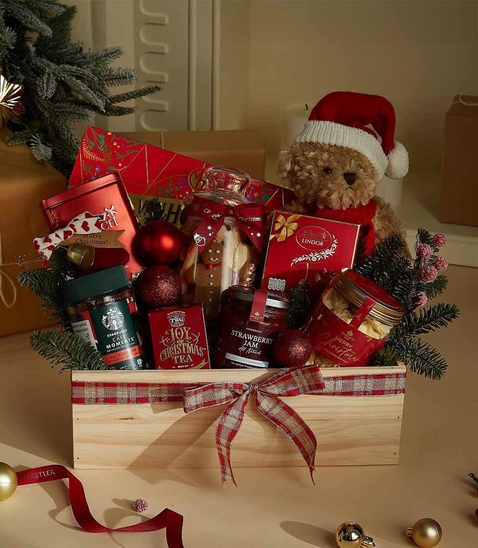 Festive wooden gift hamper featuring Lindt chocolates, holiday cookies, Christmas tea, strawberry preserves, and a plush Santa bear.