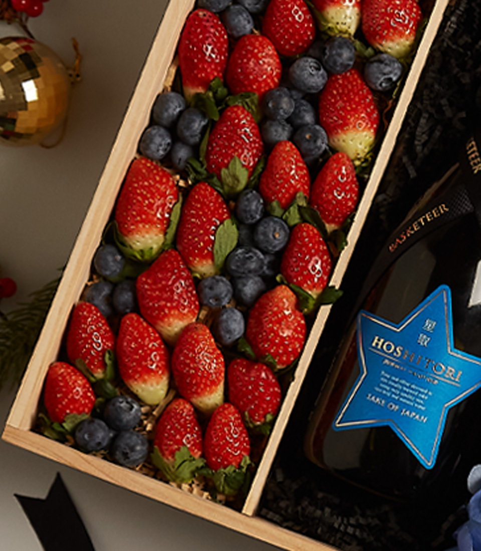 Festive gift box with strawberries, blueberries, and floral arrangements, accented with holiday decor.