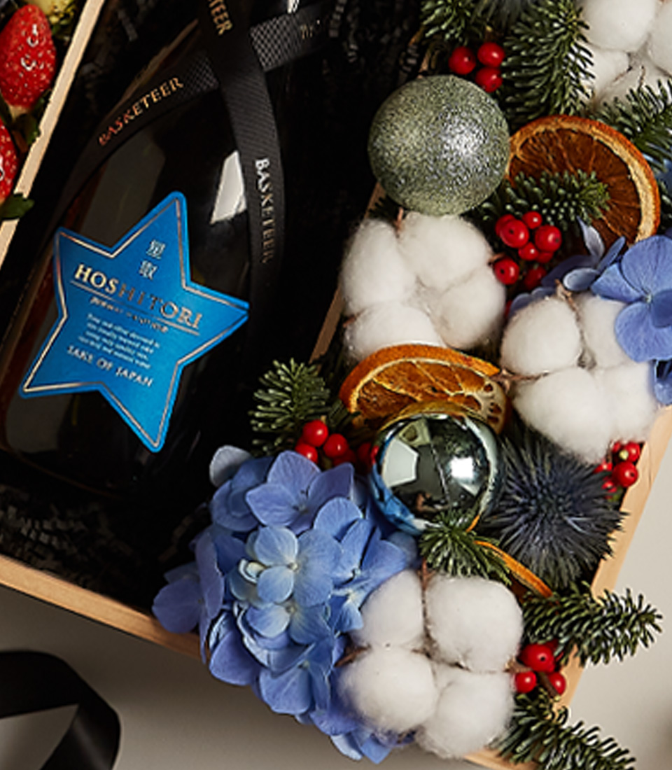 Festive gift box with strawberries, blueberries, and floral arrangements, accented with holiday decor.