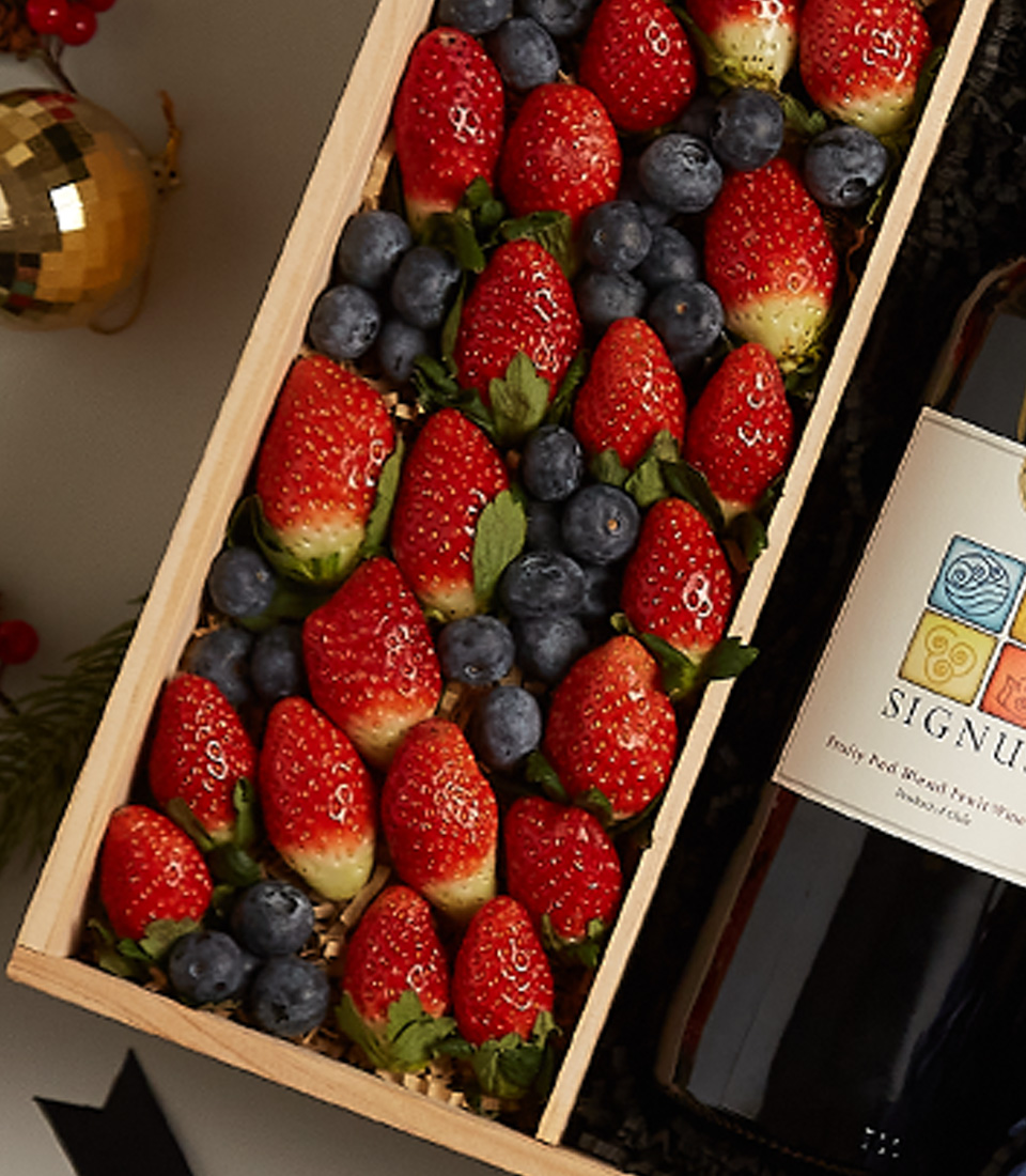 Gift box with strawberries, blueberries, and elegant floral decorations for festive celebrations.