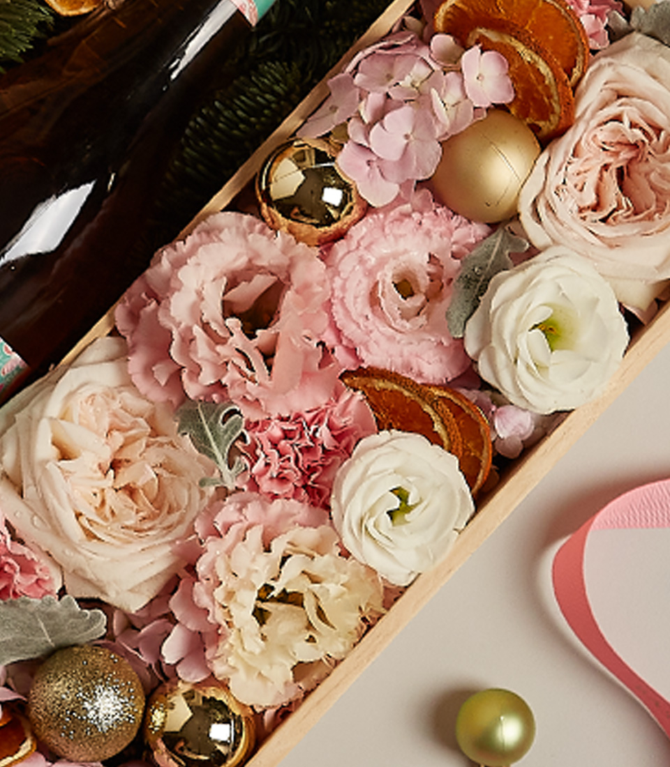 Floral gift box with pastel roses, golden accents, and festive decorations, ideal for special occasions.