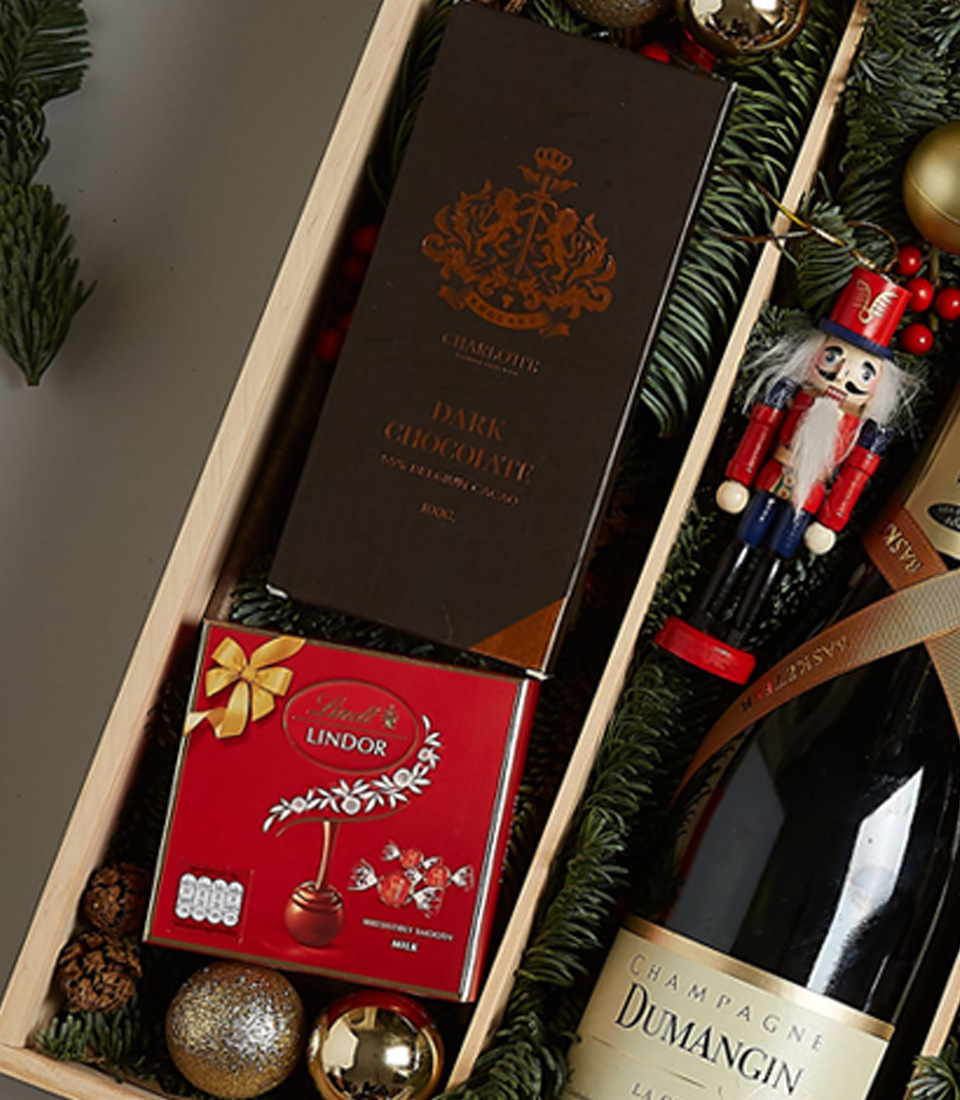 Luxurious holiday gift box featuring Champagne Dumangin, dark chocolate, Lindt pralines, festive cookies, and holiday decorations.