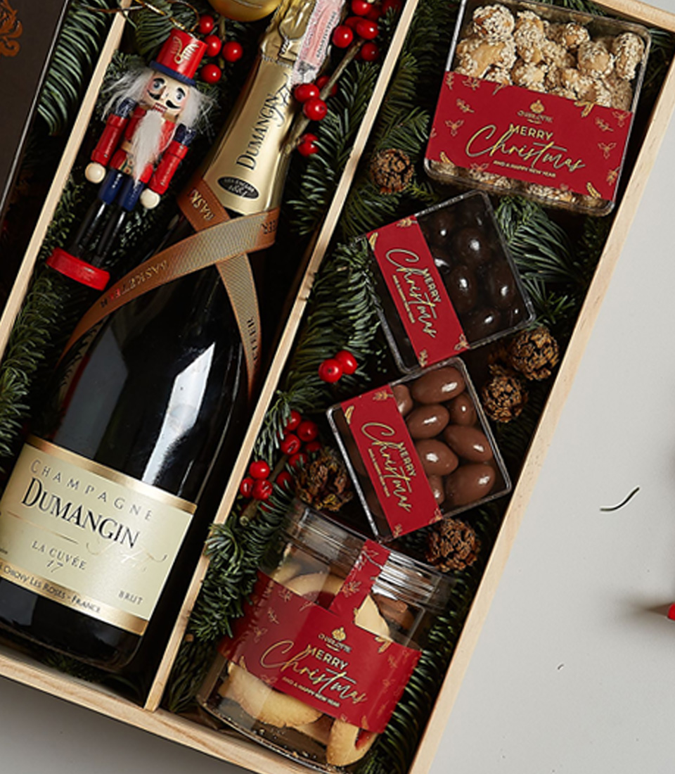 Luxurious holiday gift box featuring Champagne Dumangin, dark chocolate, Lindt pralines, festive cookies, and holiday decorations.