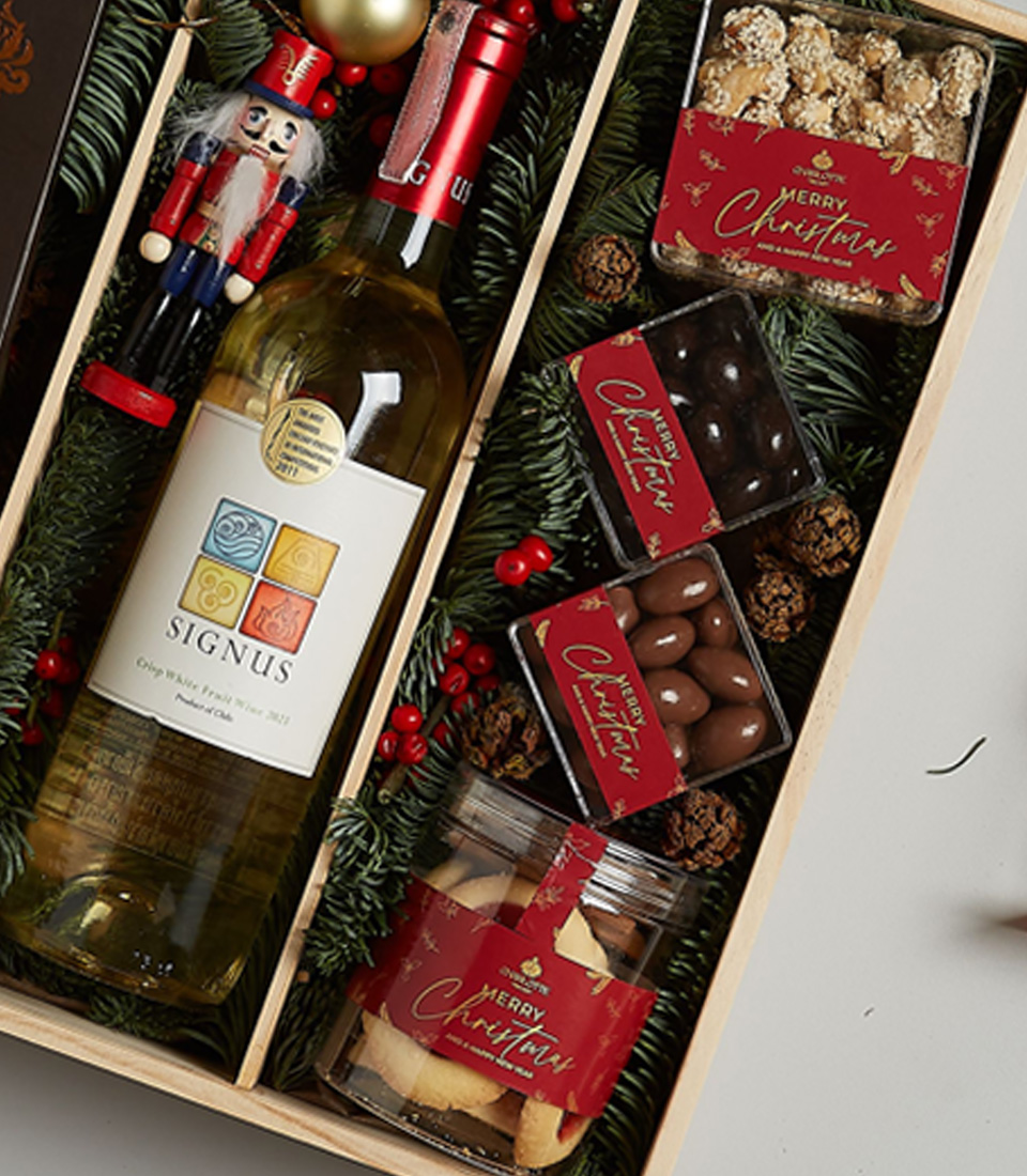 Christmas gift box with Signus white wine, dark chocolate, Lindt pralines, cookies, and festive decorations in an elegant arrangement.