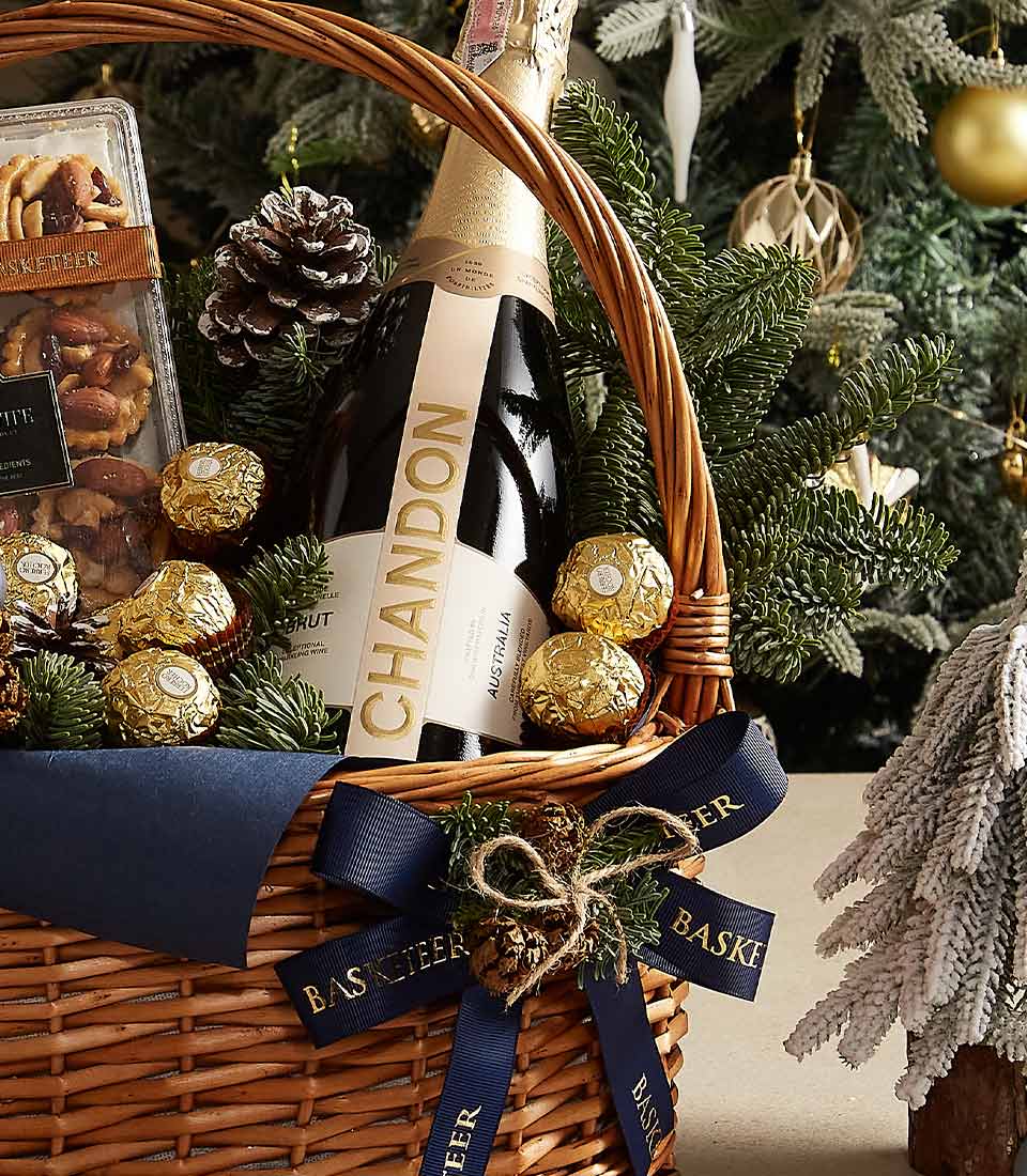 Luxury gift basket with Chandon champagne, Ferrero Rocher chocolates, gourmet cookies, and festive blue and evergreen decorations.