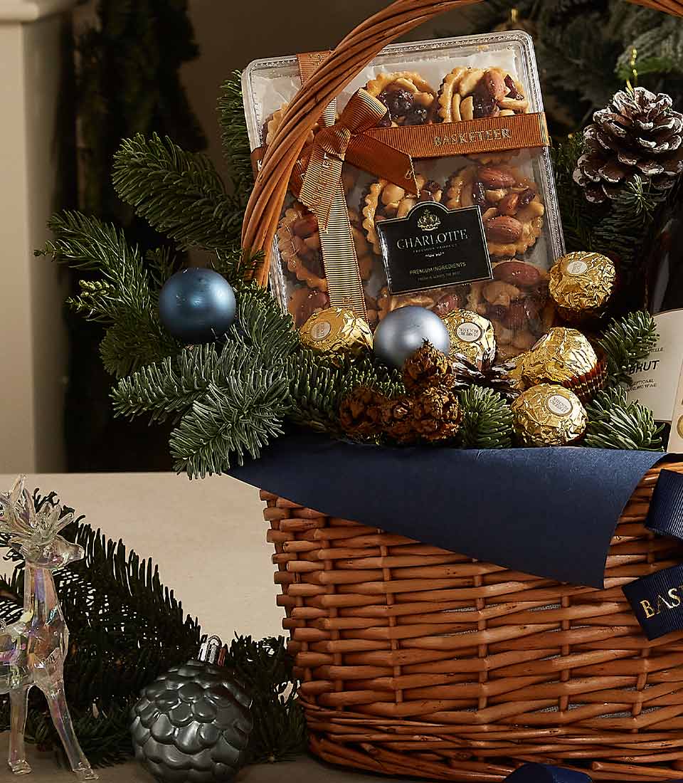 Luxury gift basket with Chandon champagne, Ferrero Rocher chocolates, gourmet cookies, and festive blue and evergreen decorations.