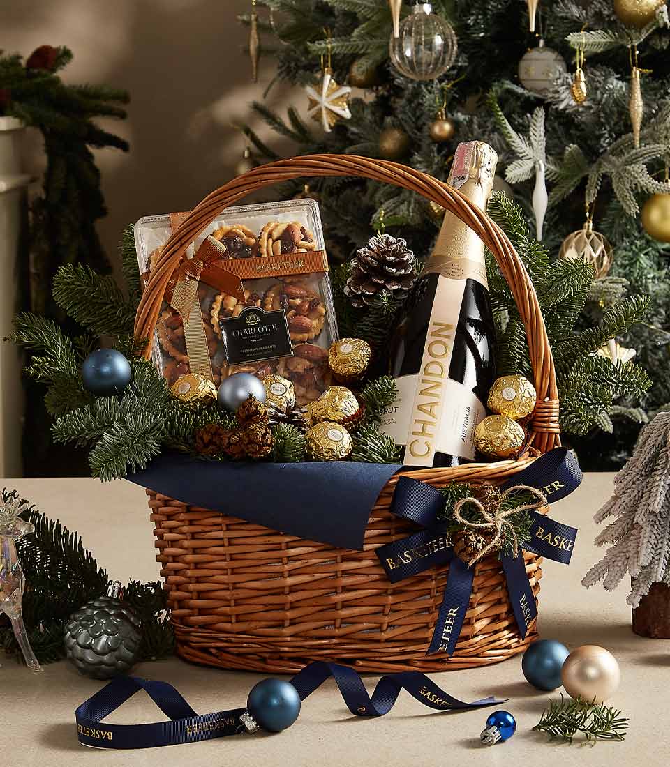 Luxury gift basket with Chandon champagne, Ferrero Rocher chocolates, gourmet cookies, and festive blue and evergreen decorations.