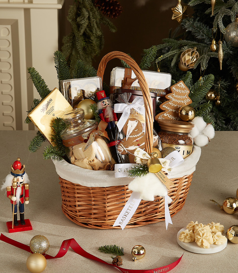 Elegant wicker basket with white and gold decorations, nutcracker, gingerbread cookies, chocolates, shortbread, and honey jars.