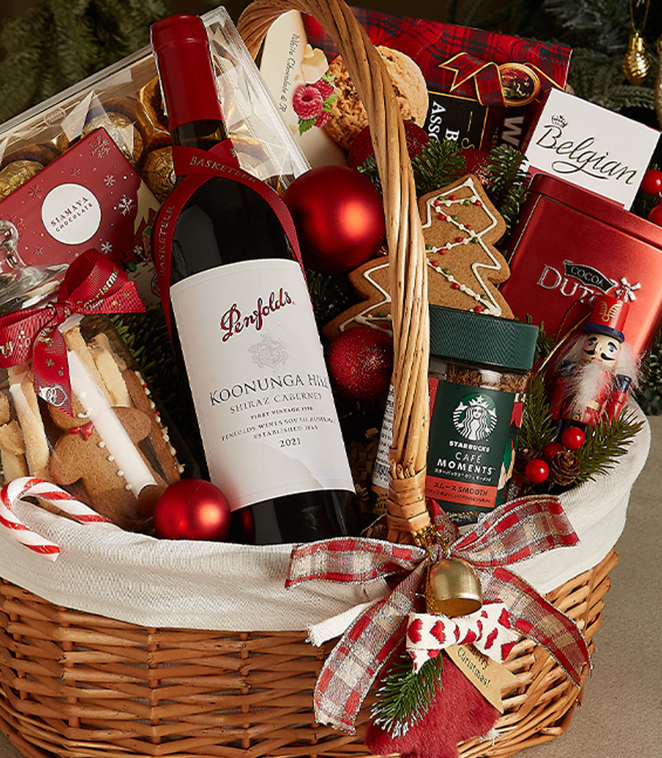 Wicker gift basket with Penfolds red wine, Belgian chocolates, holiday cookies, Starbucks coffee, gingerbread, and festive decorations.