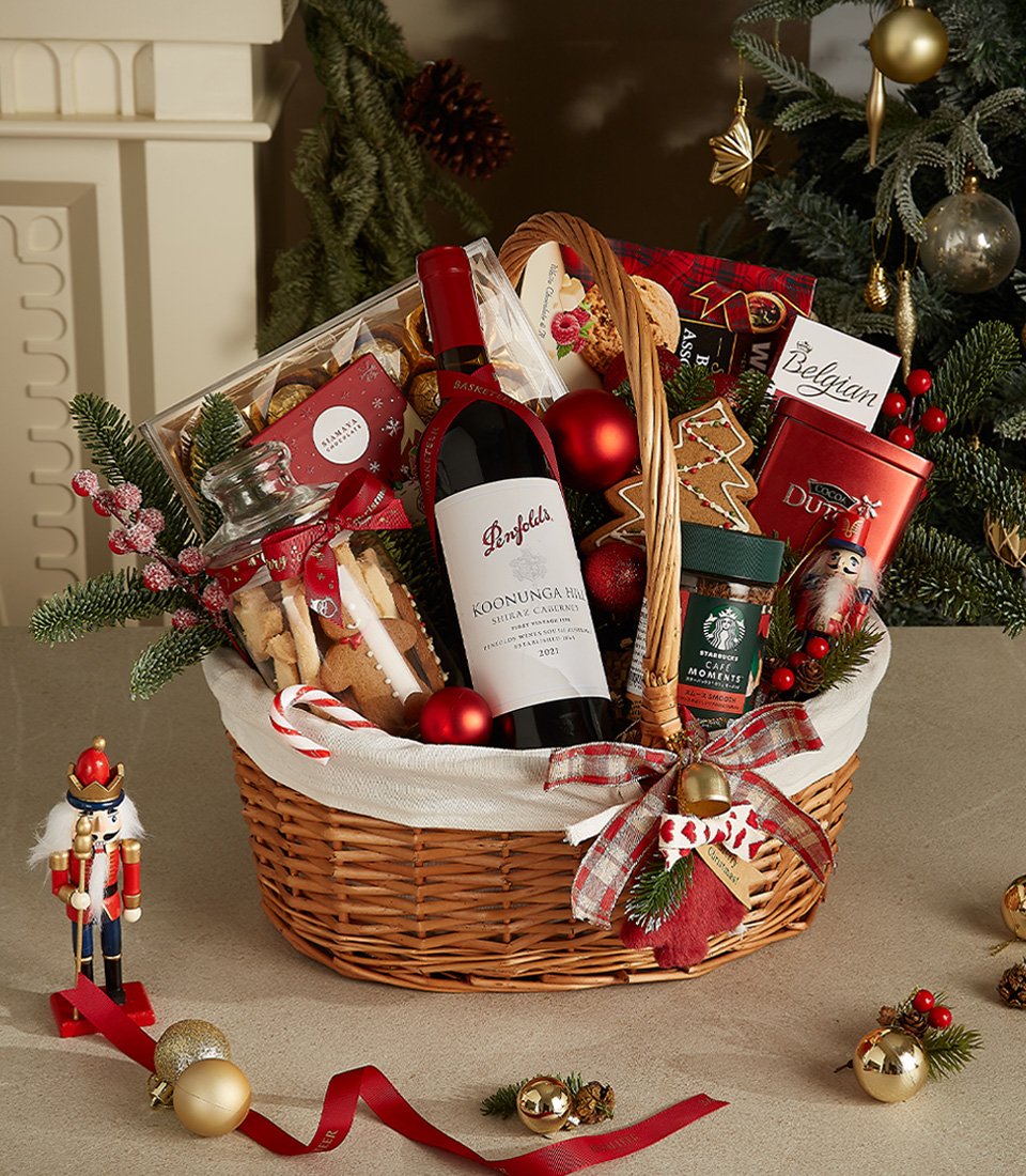 Wicker gift basket with Penfolds red wine, Belgian chocolates, holiday cookies, Starbucks coffee, gingerbread, and festive decorations.