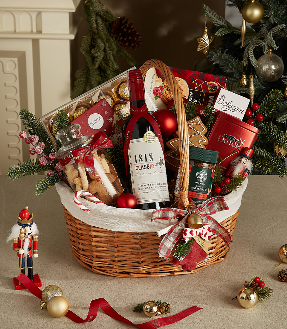 Wicker gift basket with 1818 Classic wine, Belgian chocolates, holiday cookies, Starbucks coffee, gingerbread, and festive decorations.